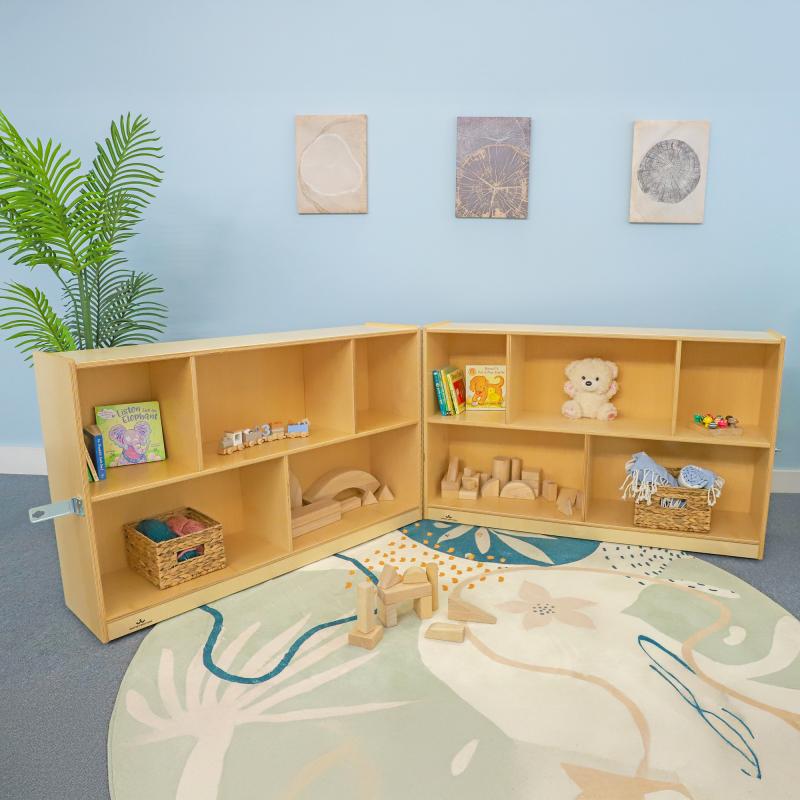 Children's playroom with wooden shelves, toys, and a rug on a light blue wall background.